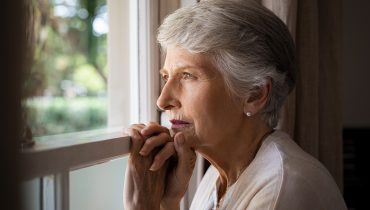 Senhora com expressão vazia olhando através da janela