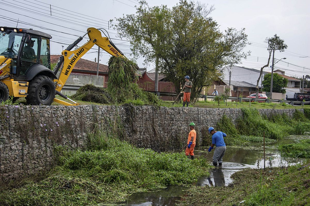 Trator e três trabalhadores retiram vegetação de dentro de um córrego no bairro Xaxim