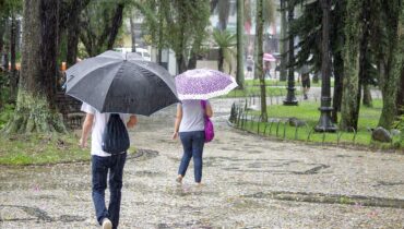 Duas pessoas com guardachuvas enfrentam chuva forte na Praça Osório, em Curitiba