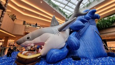 Image mostra tobogã inflável em formato de tubarão, com piscina de bolinhas de plástico no final do escorregador, tudo dentro da Praça Central do Shopping