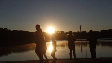 A Imagem mostra o nascer do sol em Curitiba, no Parque Barigui. Pessoas correm com roupas de frio.