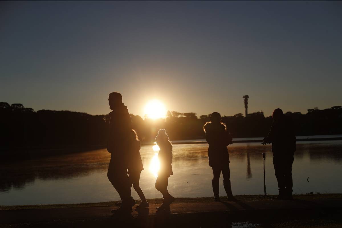 A Imagem mostra o nascer do sol em Curitiba, no Parque Barigui. Pessoas correm com roupas de frio.
