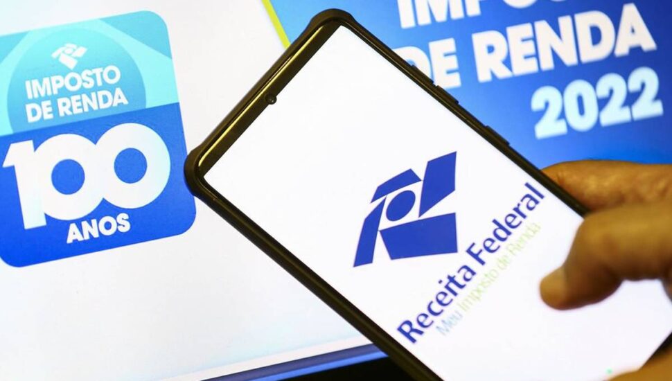Imagem mostra um celular e um computador acessando o site da Receita Federal para a consulta ao último lote da restituição do Imposto de Renda.