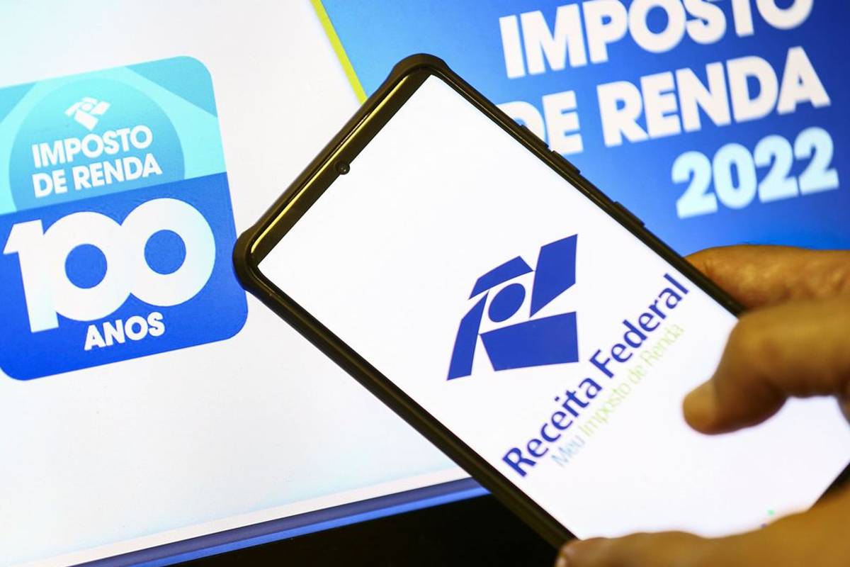 Imagem mostra um celular e um computador acessando o site da Receita Federal para a consulta ao último lote da restituição do Imposto de Renda.