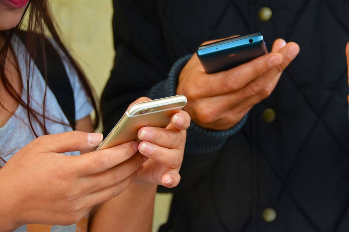 Imagem mostra duas pessoas acessando o celular para ler mensagens.