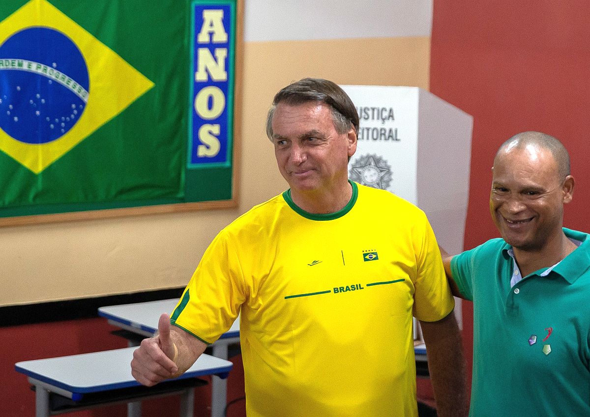 Presidente abraça correligionário perto da cabina de votação. Ele veste amarelo e faz sinal de positivo