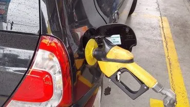 Imagem mostra um carro preto sendo abastecido com gasolina.