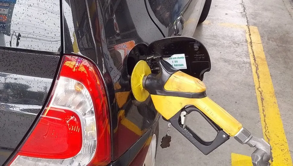 Imagem mostra um carro preto sendo abastecido com gasolina.