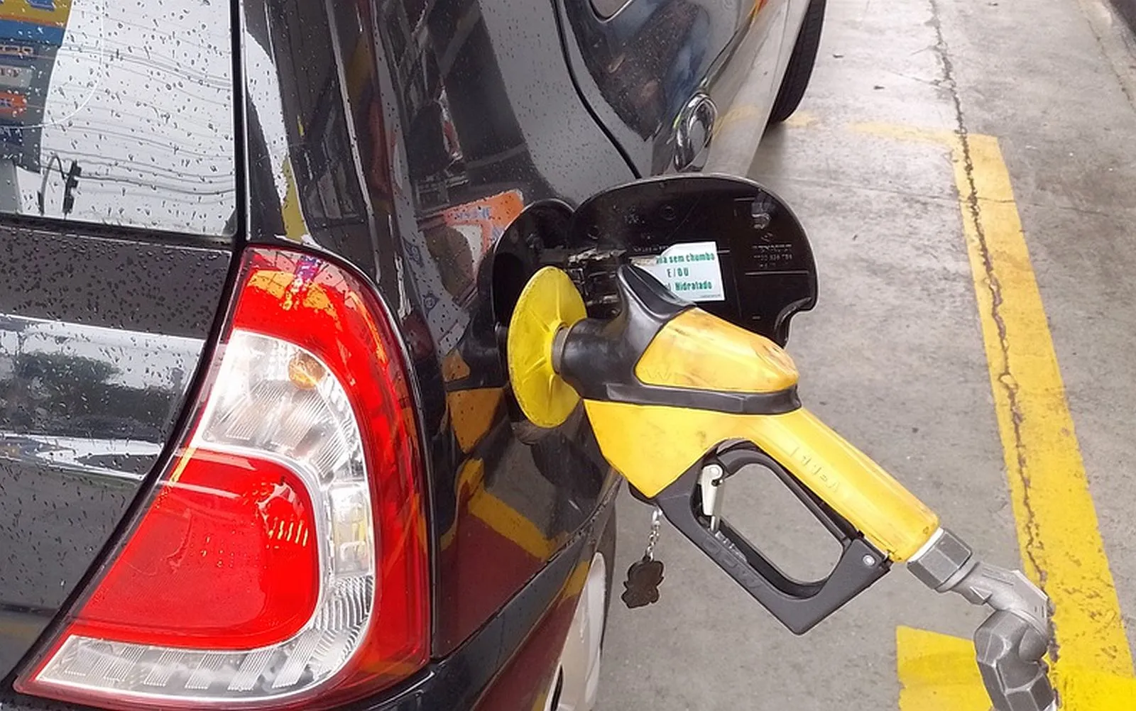 Imagem mostra um carro preto sendo abastecido com gasolina.