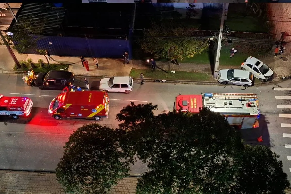 Imagem de cima mostra um acidente de trânsito com dois carros brancos e viaturas dos bombeiros.