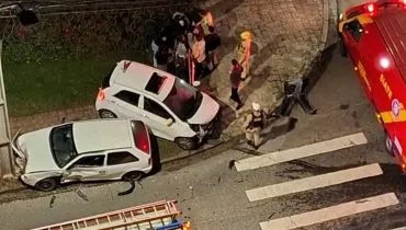 Imagem de cima mostra um acidente de trânsito com dois carros brancos e viaturas dos bombeiros.