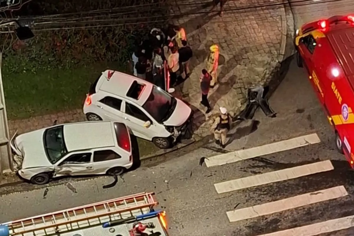 Imagem de cima mostra um acidente de trânsito com dois carros brancos e viaturas dos bombeiros.
