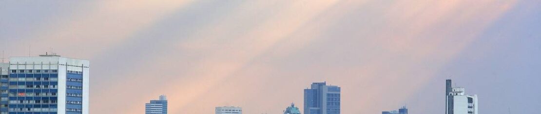 Imagem mostra Curitiba com céu fechado e os raios de sol passando pelas nuvems.