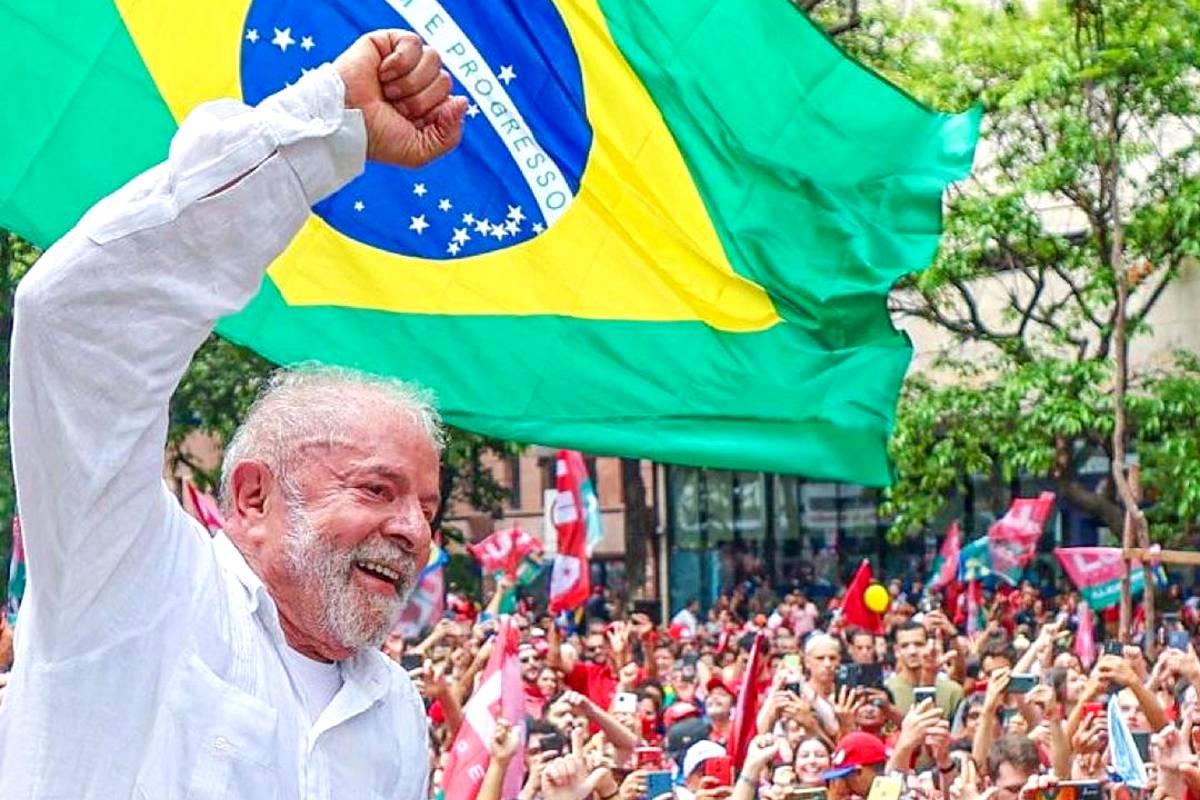 Imagem mostra candidato Lula com multidão ao fundo e bandeira do Brasil em segundo plano