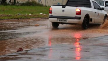 Imagem mostra um carro passando por uma área alagada.