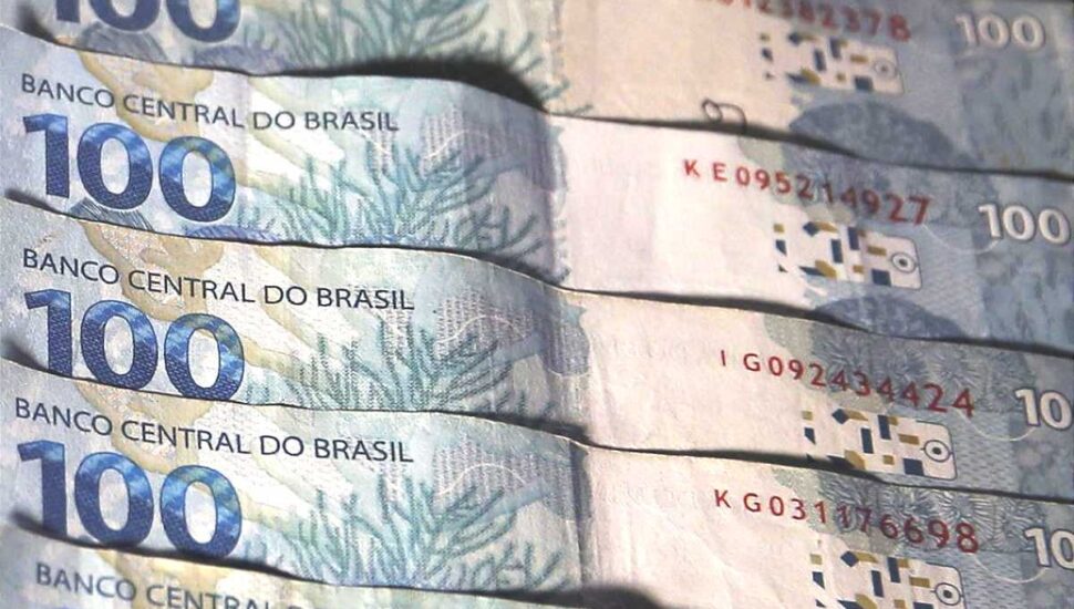 cinco notas de cem reais sobrepostas formando um leque na horizontal