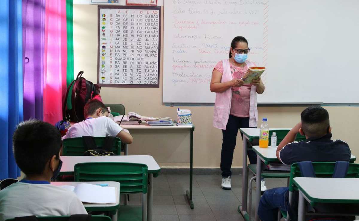 Professora de máscara dá aulas para crianças em uma escola no Brasil