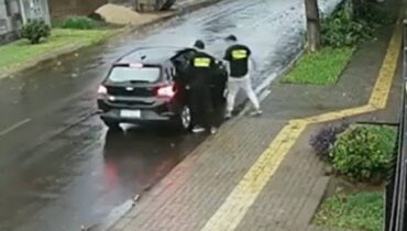 Carro preto com dois homens ao lado utilizando uma camiseta fingindo serem da Polícia Federal
