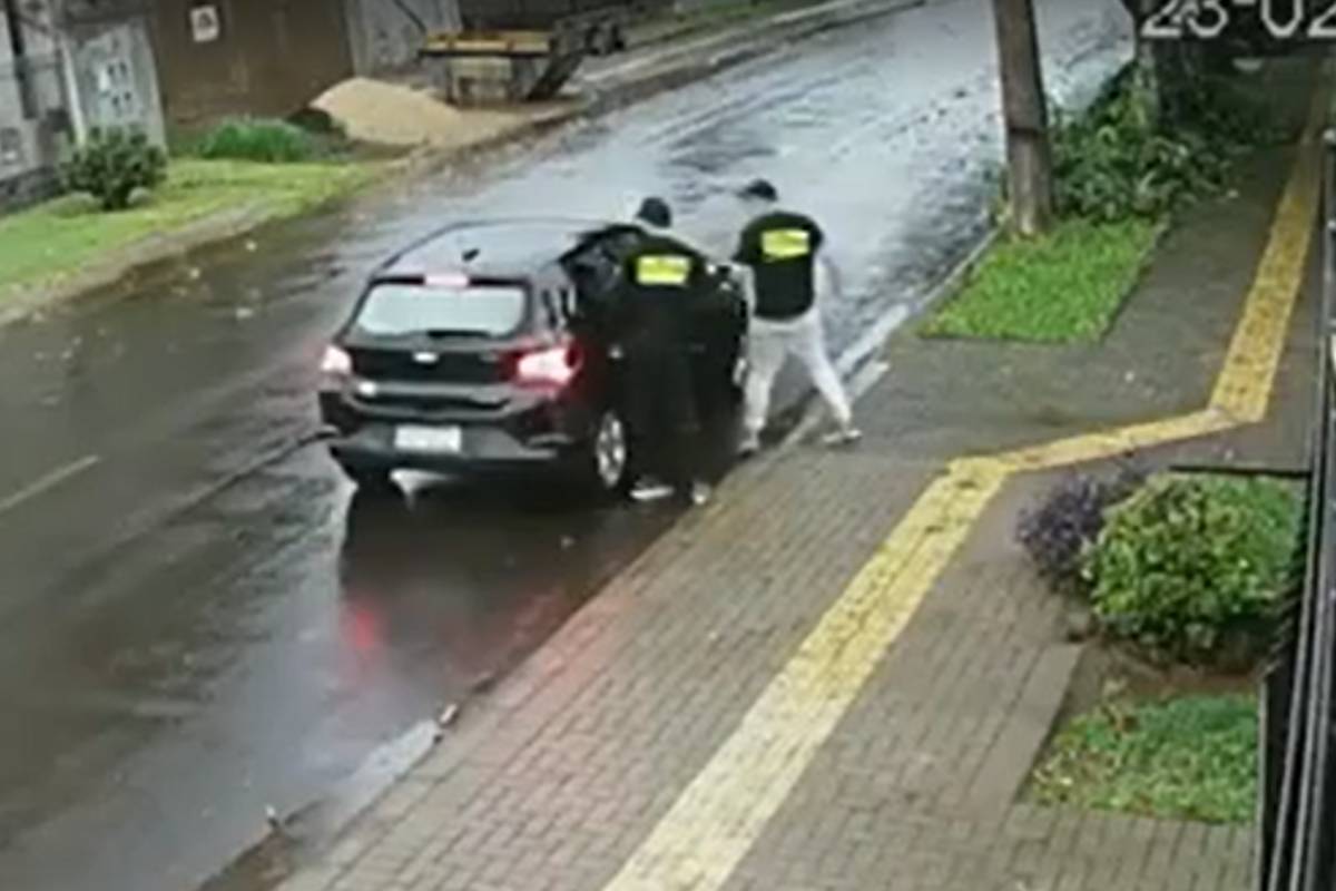 Carro preto com dois homens ao lado utilizando uma camiseta fingindo serem da Polícia Federal