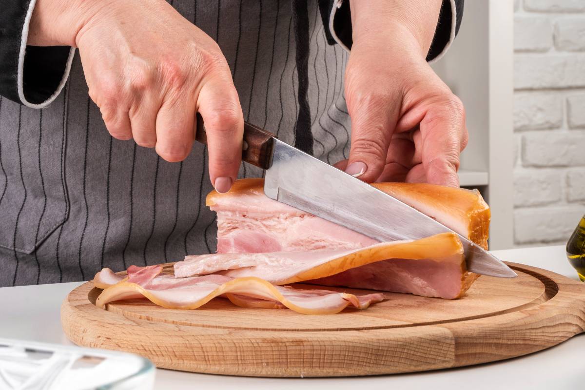 Mulher corta uma bela peça de bacon com uma faca