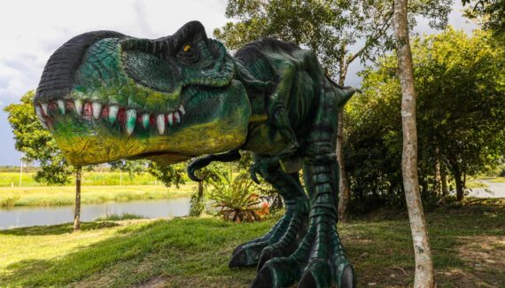 No detalhe, um tiranossauro rex no meio do Parque das Águas de Pinhais