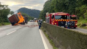 BR-277 com caminhão incendiado no meio da pista e caminhões dos bombeiros em atendimento. Rodovia está interditada.