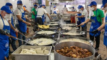 imagem mostra voluntários cozinhando polenta frango em uma cozinha industrial.