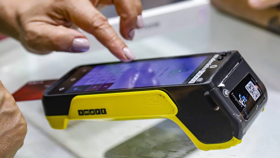 Imagem mostra uma mulher digitando a senha em uma máquina de cartão de débito e crédito.