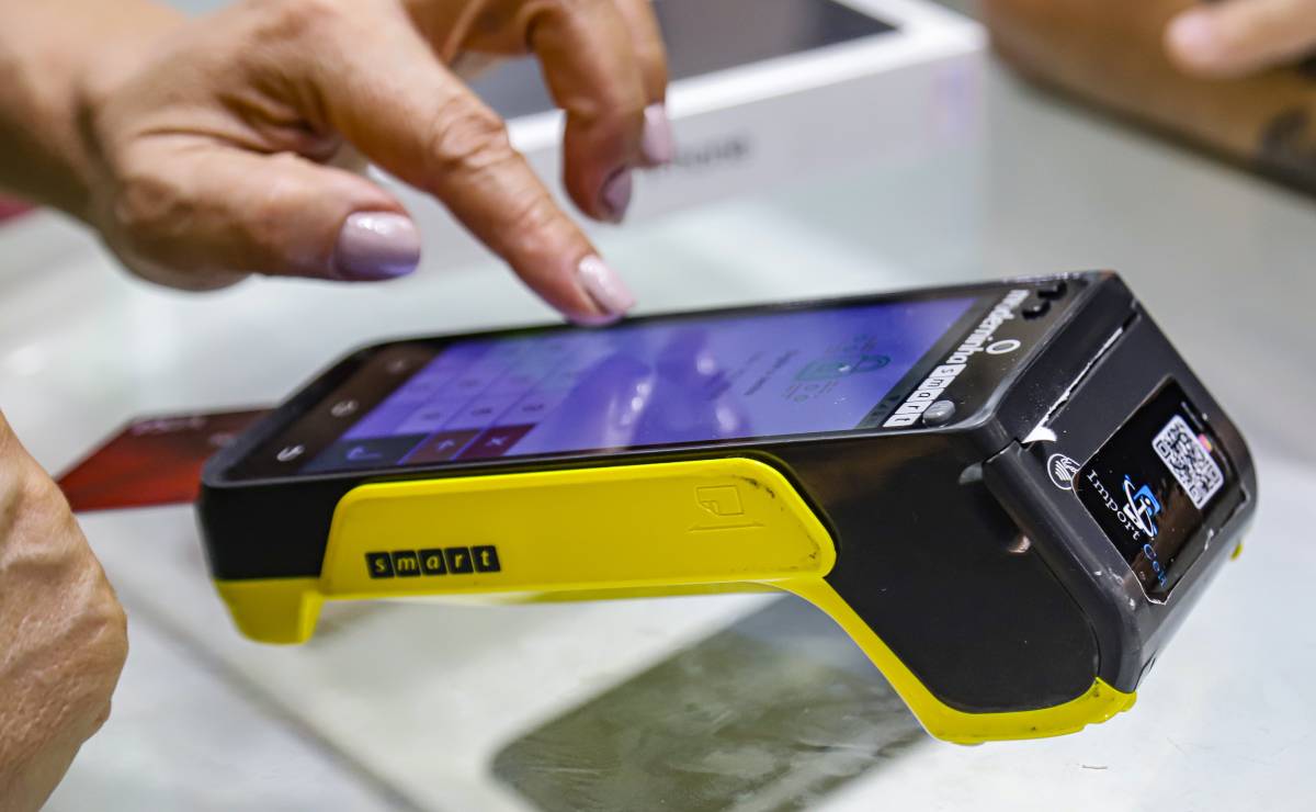 Imagem mostra uma mulher digitando a senha em uma máquina de cartão de débito e crédito.