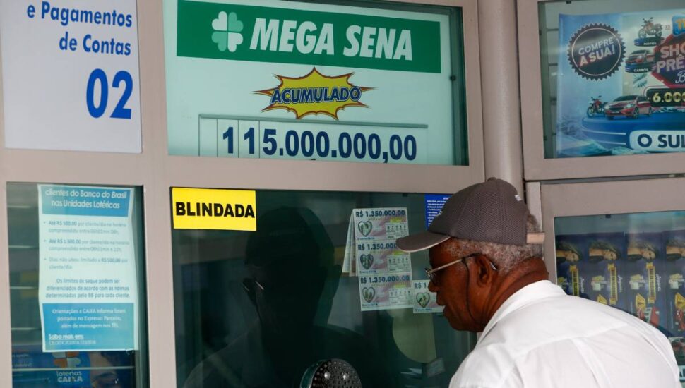 Imagem mostra um apostador em um guichê de uma lotérica e a informação da Mega Sena acumulada em cima.