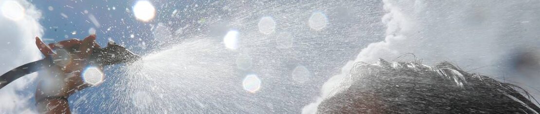 Imagem mostra uma mulher tomando um banho de mangueira com sol ao fundo