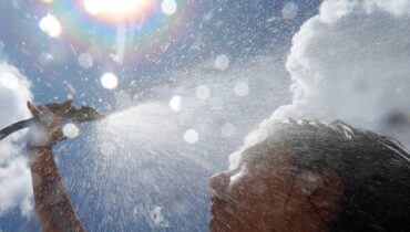 Imagem mostra uma mulher tomando um banho de mangueira com sol ao fundo