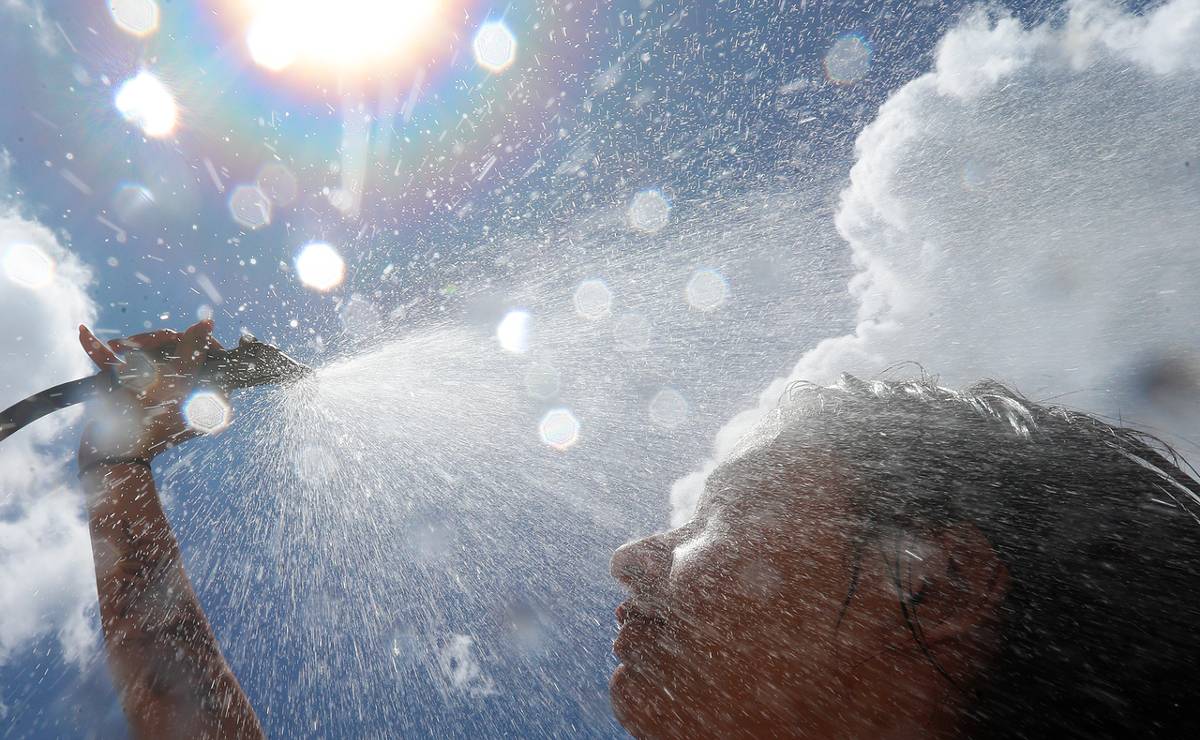 Imagem mostra uma mulher tomando um banho de mangueira com sol ao fundo