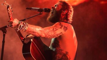 Imagem mostra o cantor Post Malone com um violão em um show ao vivo.