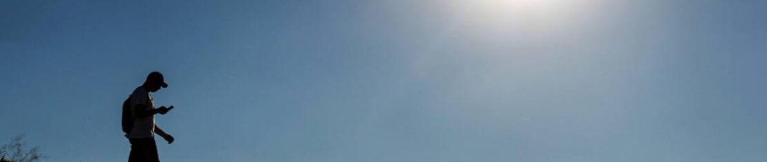 Imagem mostra um homem caminhando com um sol escaldante ao fundo