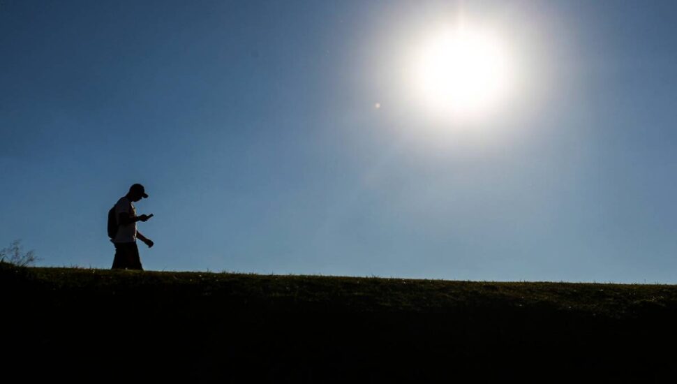 Imagem mostra um homem caminhando com um sol escaldante ao fundo
