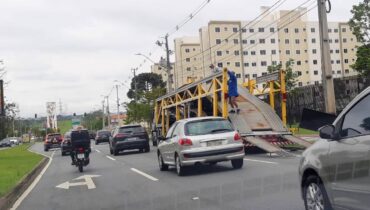 Imagem mostra uma cegonheira descarregando carros em uma das faixas da Avenida Comendador Franco, em Curitiba.