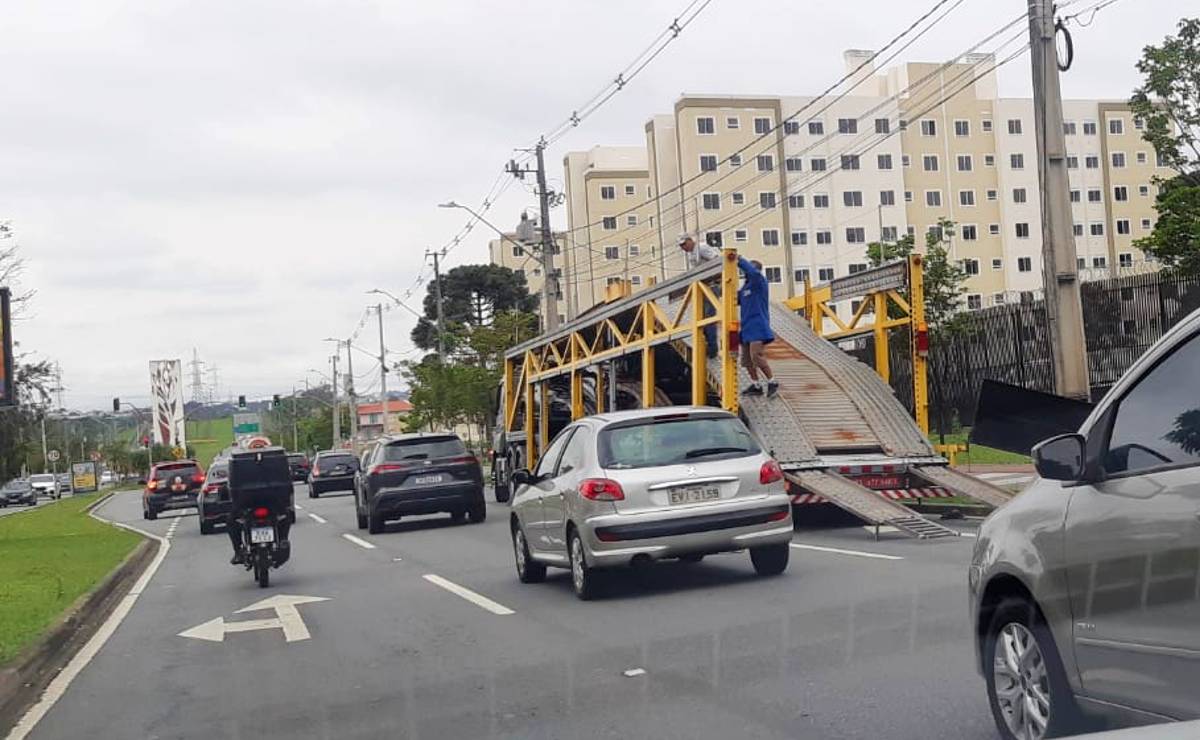 Imagem mostra uma cegonheira descarregando carros em uma das faixas da Avenida Comendador Franco, em Curitiba.