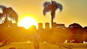 Imagem mostra o sol no parque bacacheri, em Curitiba. Sol se esconde entre os prédios.