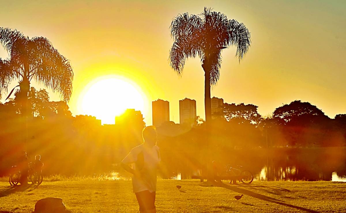 Imagem mostra o sol no parque bacacheri, em Curitiba. Sol se esconde entre os prédios.