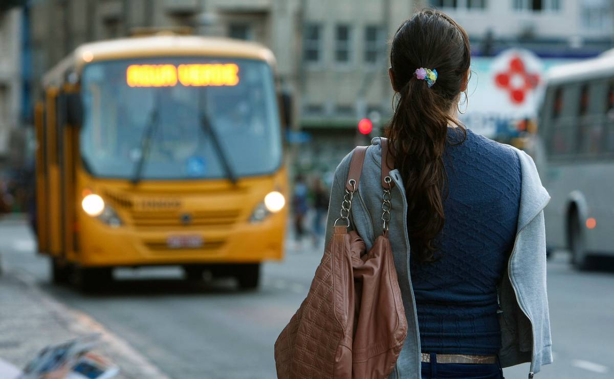 Imagem mostra um ônibus de Curitiba com uma estudante esperando para embarcar,