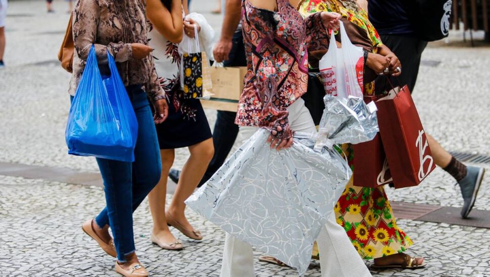 Imagem mostra mulheres com sacolas de lojas andando pelo centro de Curitiba.