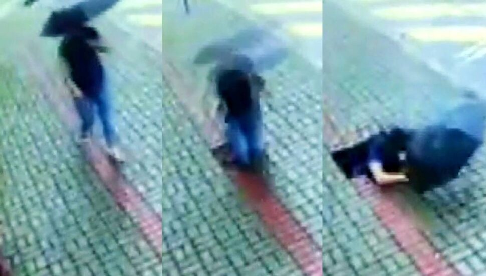 Imagem mostra uma mulher andando em uma calçada com um guarda chuva e sendo engolida por um buraco