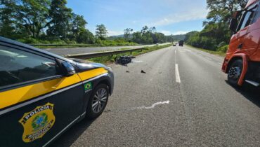 Imagem mostra a BR-277 com uma viatura na faixa esquerda e um caminhão na faixa da direita. A imagem de um sol brilhando num dia de céu limpo e calor