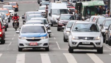 Imagem mostra carros circulando por uma rua movimentada de Curitiba.