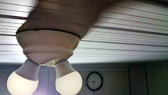 imagem mostra um lustre com duas lâmpadas apagadas com um relógio ao fundo