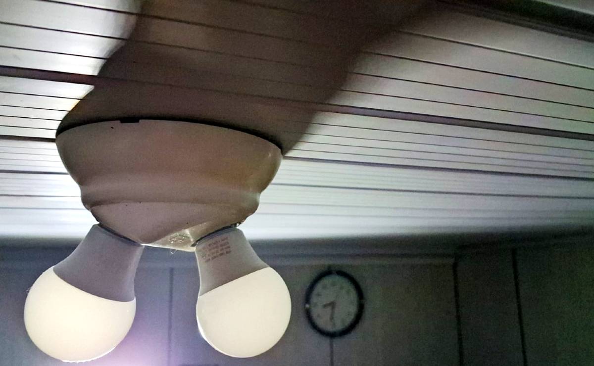 imagem mostra um lustre com duas lâmpadas apagadas com um relógio ao fundo