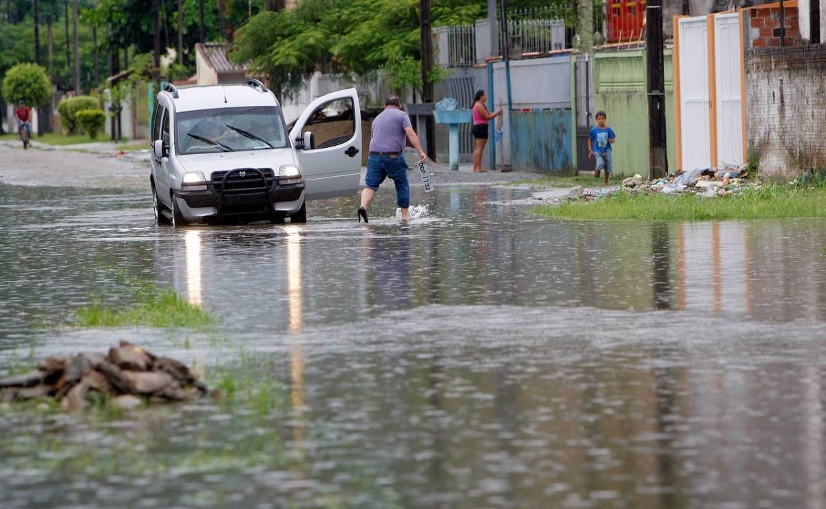 Imagem mostra um alagamento no litoral do Paraná e um homem resgatando a placa de um carro que caiu com o alagamento