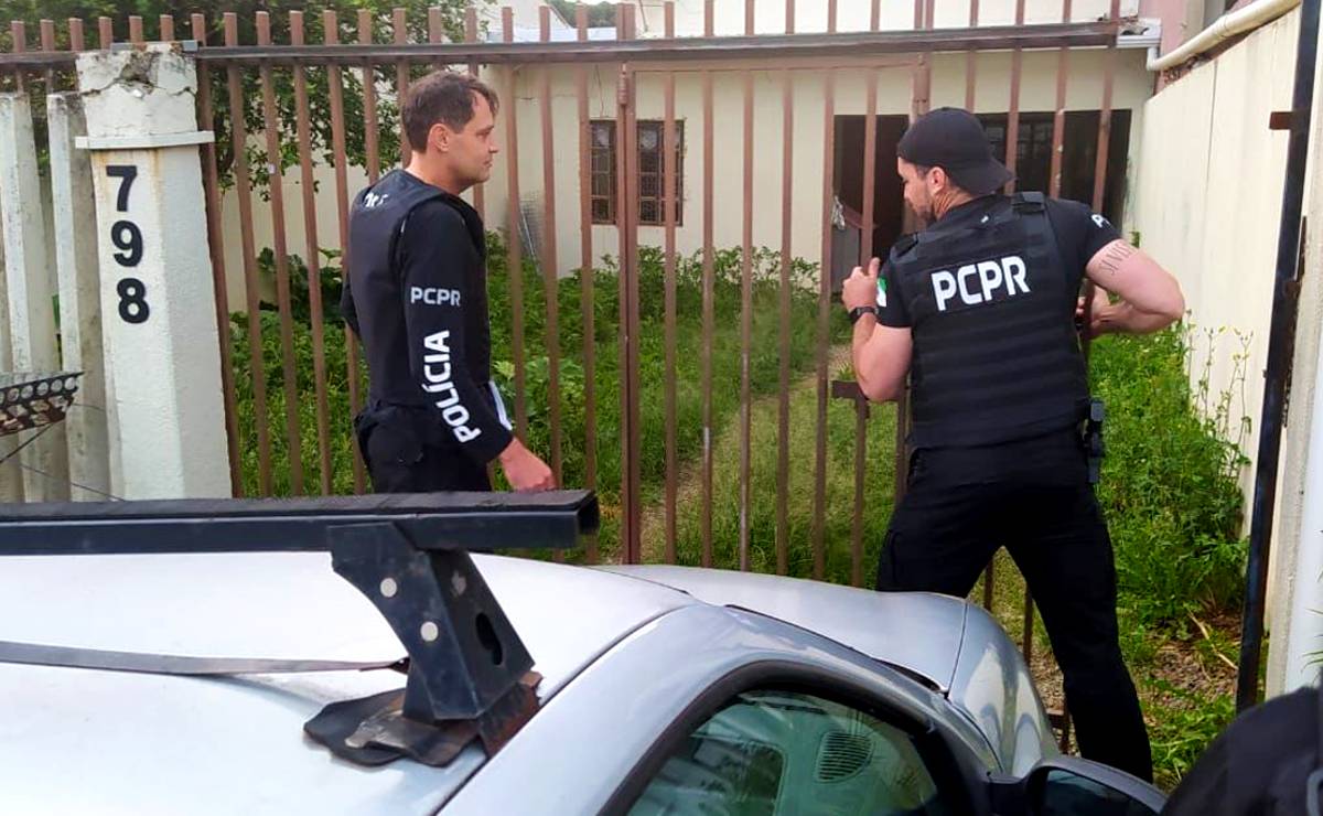 Imagem mostra policiais arrombando o portão de uma casa com grama alta e mal cuidada