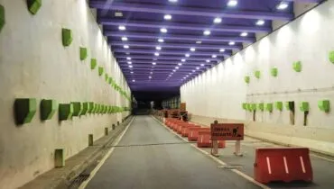 Imagem mostra um trecho da trincheira entre o Bairro Alto e o Bacacheri, em Curitiba. Está de noite e as luzes têm destaque. A trincheira é roxa com peças em verde.